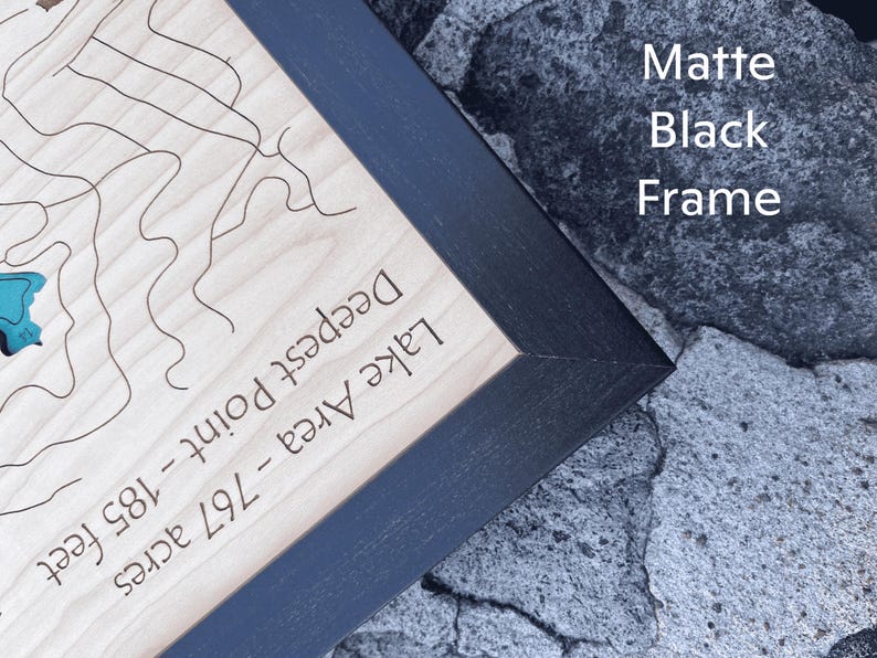 May include: A wooden map of a lake with a black matte frame. The map shows the lake's area, deepest point, and the depth in feet. The text on the map reads "Lake Area - 79.7 acres, Deepest Point - 185 feet".