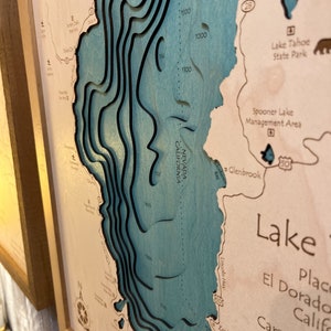 May include: A wooden map of Lake Tahoe with depth contours carved into the wood. The map is painted in shades of blue and brown. The map includes the text "Lake Tahoe State Park", "Spooner Lake Management Area", and "Glenbrook".
