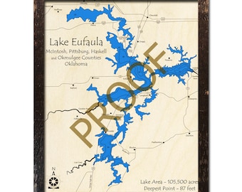 May include: A map of Lake Eufaula in Oklahoma, showing the lake's shape and depth contours. The map is framed in a dark wood frame. The text "Lake Eufaula" is printed in brown at the top of the map. The text "McIntosh, Pittsburg, Haskell and Okmulgee Counties Oklahoma" is printed below the lake name. The text "Lake Area - 105,500 acres" and "Deepest Point - 87 feet" is printed at the bottom of the map.