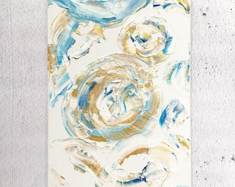 May include: Abstract painting with swirling blue, gold, and white paint on a white canvas. The painting is signed "Wildflower Day".