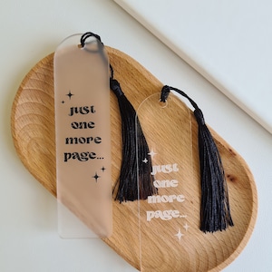 May include: Two clear acrylic bookmarks with black tassels. Each bookmark has the text "Just one more page..." printed in black with a star design.