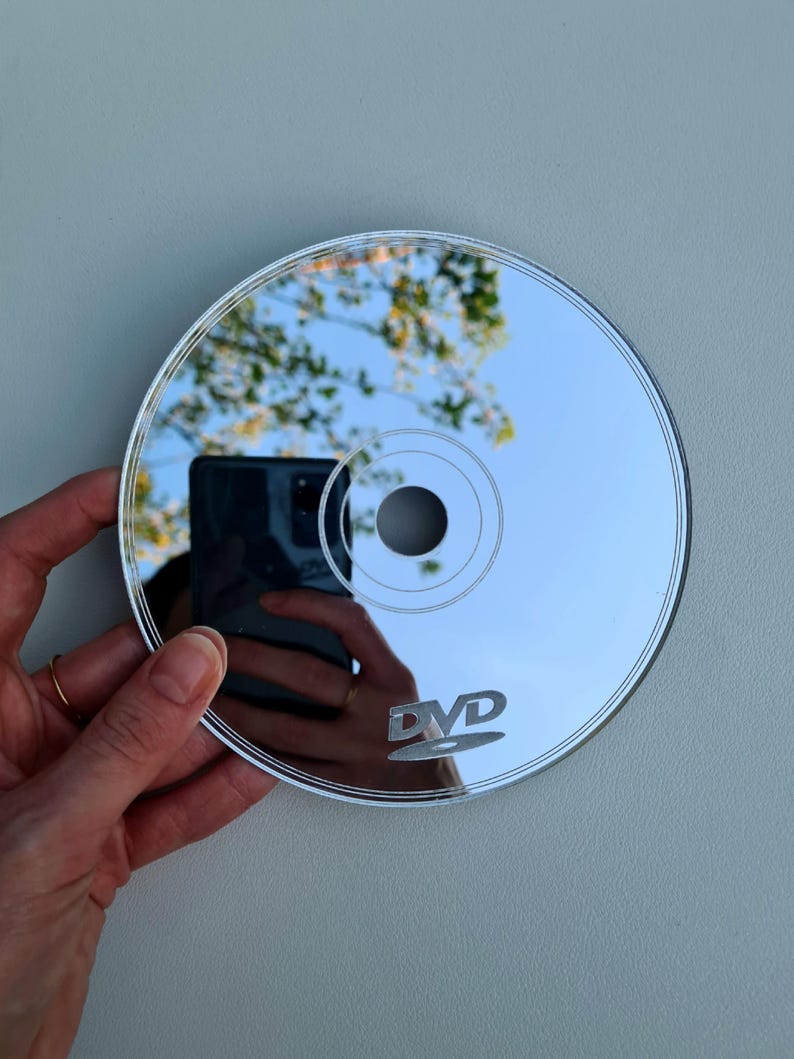 May include: A reflective DVD disc with the word "DVD" printed on it. The disc reflects a blue sky and tree branches. The disc is held by a person.