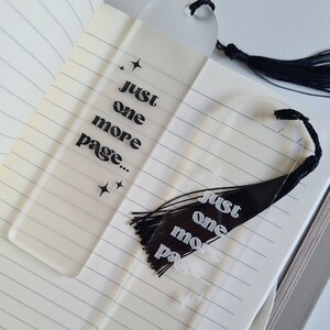 May include: Two clear acrylic bookmarks with black tassels. The bookmarks have the text "Just one more page..." printed on them in a retro font.