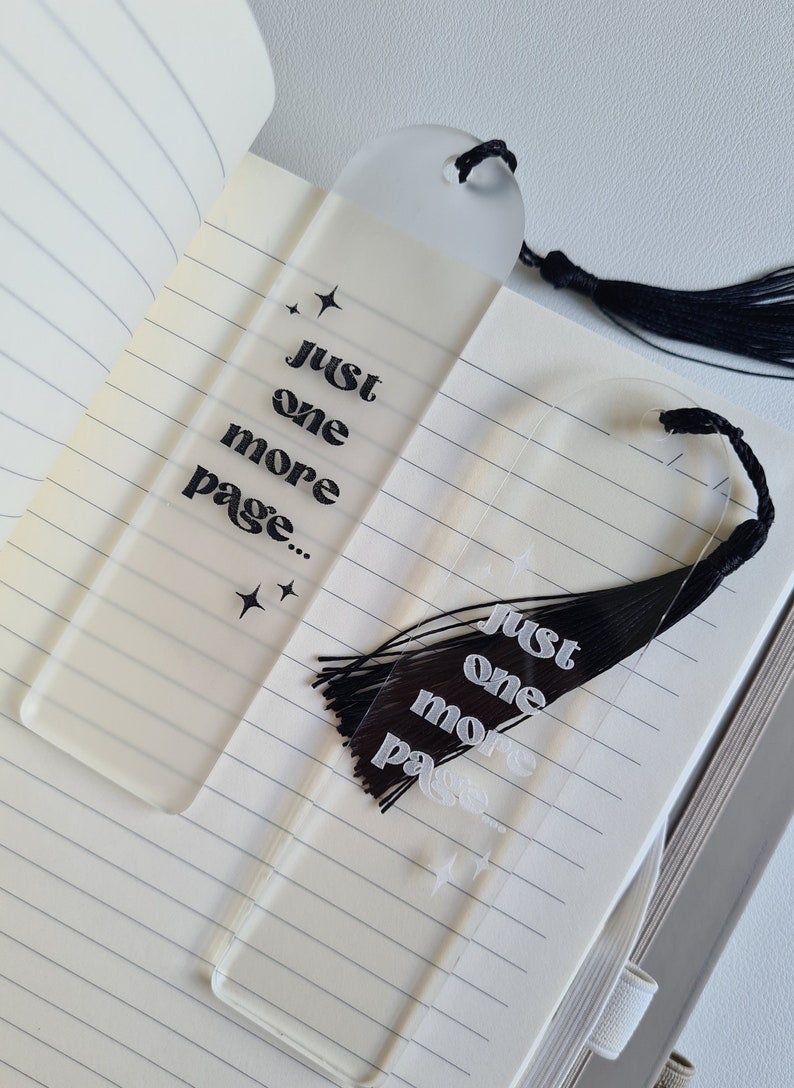 May include: Two clear acrylic bookmarks with black tassels. The bookmarks have the text "Just one more page..." printed on them in a retro font.