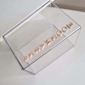 May include: A clear plastic box with the word "remarkable" spelled out in beige letters.