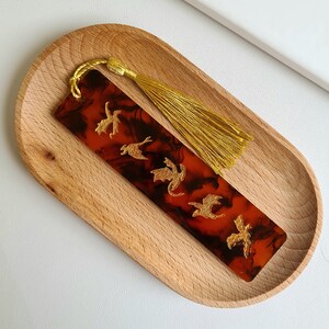 K&ouml;nnte beinhalten: Ein Lesezeichen aus rotem und schwarzem Harz mit einem goldenen Quasten und einem Design aus f&uuml;nf goldenen Drachen.