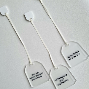 Puede incluir: Cuatro marcap&aacute;ginas transparentes con forma de bolsita de t&eacute; con cuerdas blancas. Cada marcap&aacute;ginas tiene una frase diferente impresa en negro: "hot tea warm blanket good book", "caffeinated and captivated" y "this book is not tea".