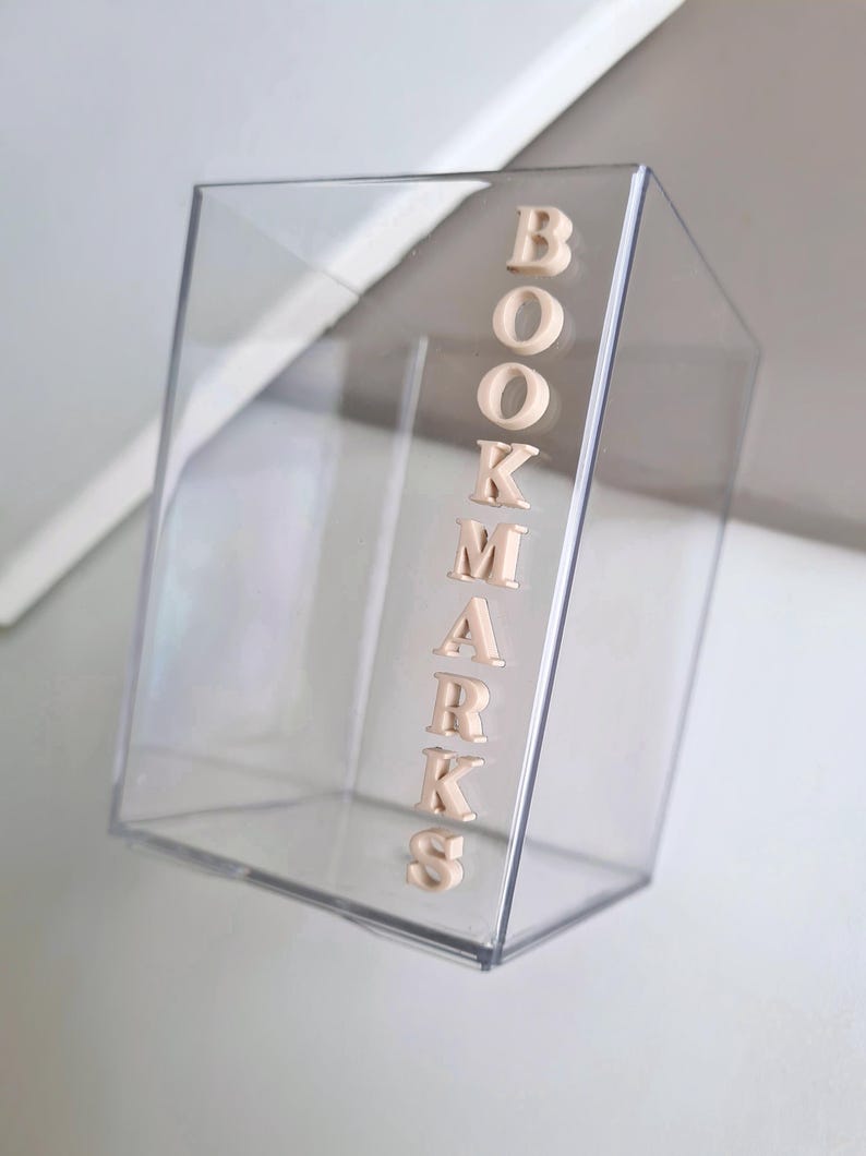 May include: A clear acrylic box with the word "BOOKMARKS" spelled out in beige letters on the side.