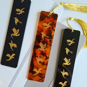 K&ouml;nnte beinhalten: Zwei Lesezeichen mit goldenen Drachenmotiven. Ein Lesezeichen ist schwarz mit goldenen Drachen und das andere ist braun mit goldenen Drachen.