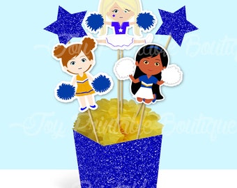 May include: Cheerleader centrepiece with three figures, two stars, and pom-poms. The figures are wearing blue and yellow uniforms. The centrepiece is in a blue glitter box with the word "Cheer" on the front. Centrepiece Cheer.