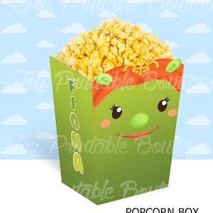 May include: A green and red popcorn box featuring a cartoon face of Fiona from Shrek. The box says "Fiona" on the side and "POPCORN BOX SHREK" at the bottom.
