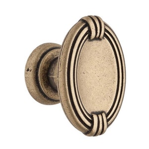 May include: An antique brass cabinet knob with an oval shape and a decorative, raised, concentric ring design.