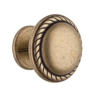 Może przedstawiać: Złoty gałka do szafki z wzorem sznurka wok&oacute;ł krawędzi. Gałka ma okrągły kształt i lekko wypukły środek.