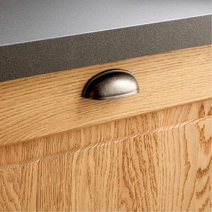 May include: A close-up of a cabinet door with a wood grain finish. The door has a silver-toned cup-shaped pull handle.