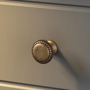 May include: A round, antique gold-toned cabinet knob with a decorative, raised, beaded edge.
