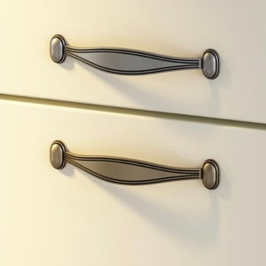 May include: Two silver drawer pulls with a curved design and oval-shaped ends. The pulls are mounted on a white cabinet door.