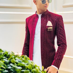 Puede incluir: Un hombre lleva una chaqueta de terciopelo burdeos con una camisa blanca y un pa&ntilde;uelo de bolsillo dorado. La chaqueta tiene un patr&oacute;n texturizado y est&aacute; adornada con lentejuelas.