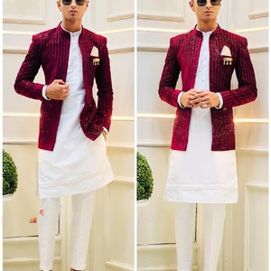Puede incluir: Un hombre con un blazer rojo burdeos con lentejuelas sobre una camisa blanca de manga larga y pantalones blancos. Lleva zapatos negros y gafas de sol.