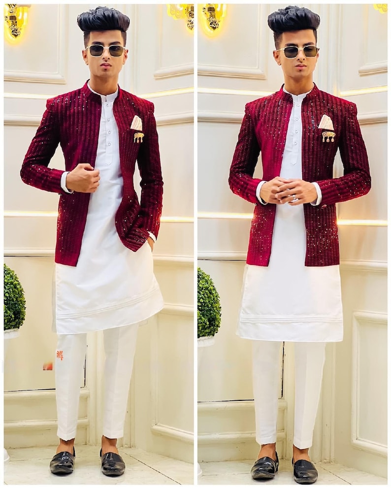 Puede incluir: Un hombre con un blazer rojo burdeos con lentejuelas sobre una camisa blanca de manga larga y pantalones blancos. Lleva zapatos negros y gafas de sol.