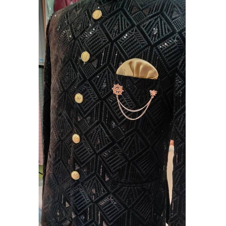 May include: A black velvet jacket with a geometric pattern and gold buttons. The jacket has a pocket on the left side with a gold chain and a decorative pin.