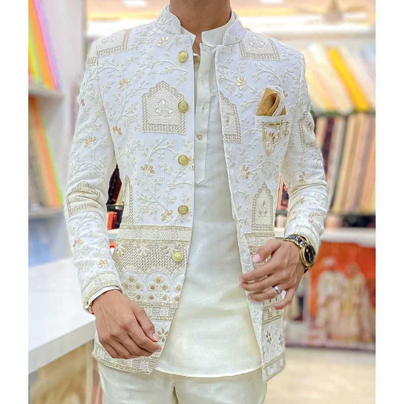 May include: A white blazer with gold embroidery and buttons. The blazer has a mandarin collar and a pocket on the left side.