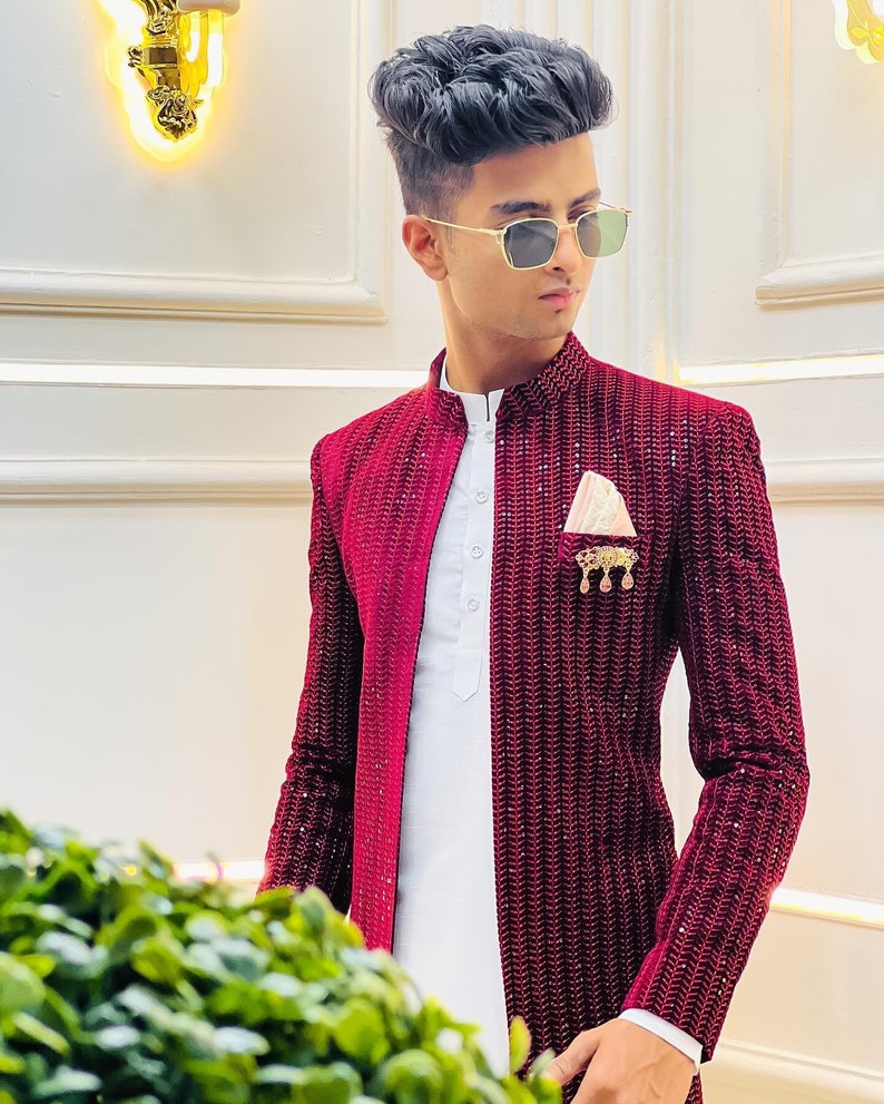 Puede incluir: Un hombre lleva una chaqueta de terciopelo burdeos con una camisa blanca y un pa&ntilde;uelo de bolsillo dorado. La chaqueta tiene un patr&oacute;n texturizado y est&aacute; adornada con lentejuelas.