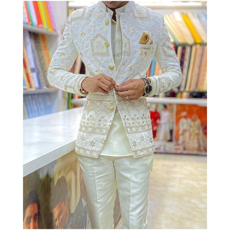 May include: A white blazer with gold embroidery and a white button-up shirt. The blazer has a mandarin collar and a single button closure. The shirt has a mandarin collar and a button-up closure. The blazer and shirt are both made of a lightweight fabric.