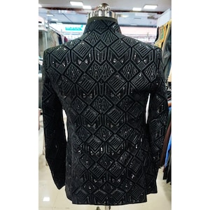 May include: A black blazer with a geometric pattern made of sequins. The blazer has a stand-up collar and long sleeves.