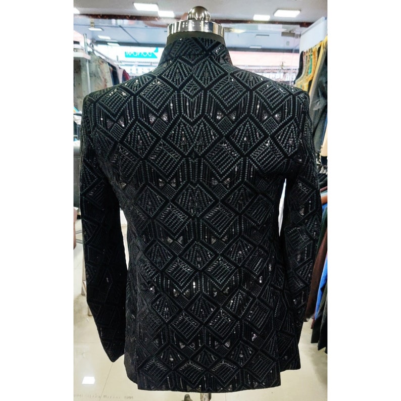 May include: A black blazer with a geometric pattern made of sequins. The blazer has a stand-up collar and long sleeves.