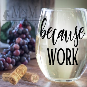 May include: A clear glass wine glass with the text "because work" printed on the side. The glass is filled with white wine and is sitting on a wooden table.