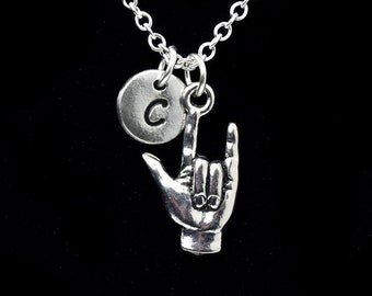 May include: Silver necklace with a charm of a hand signing the letter 'I' in American Sign Language and a small round charm with the letter 'C' engraved on it.
