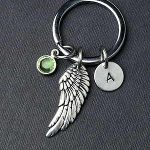 以下が含まれることがあります： 緑色の宝石、銀の天使の羽根のチャーム、そしてAの文字が刻まれた銀のチャームが付いた銀のキーホルダーです。