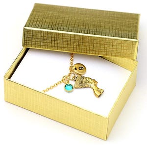 May include: A gold necklace with a turquoise charm, an initial charm, and an Egyptian-style charm in a gold gift box.
