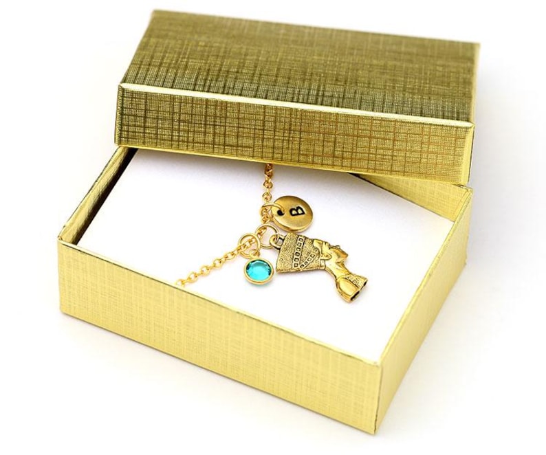 May include: A gold necklace with a turquoise charm, an initial charm, and an Egyptian-style charm in a gold gift box.