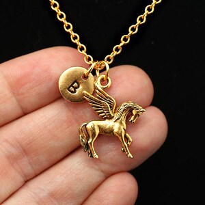 May include: Gold necklace featuring a winged horse charm and a round charm engraved with the letter "B".