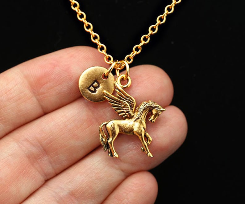 May include: Gold necklace featuring a winged horse charm and a round charm engraved with the letter "B".