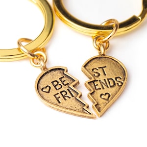 Peut inclure: Deux porte-clés dorés avec des breloques en forme de cœur qui disent "Best Friends" et "Be Friends". Les breloques sont cassées en deux, symbolisant l'amitié.