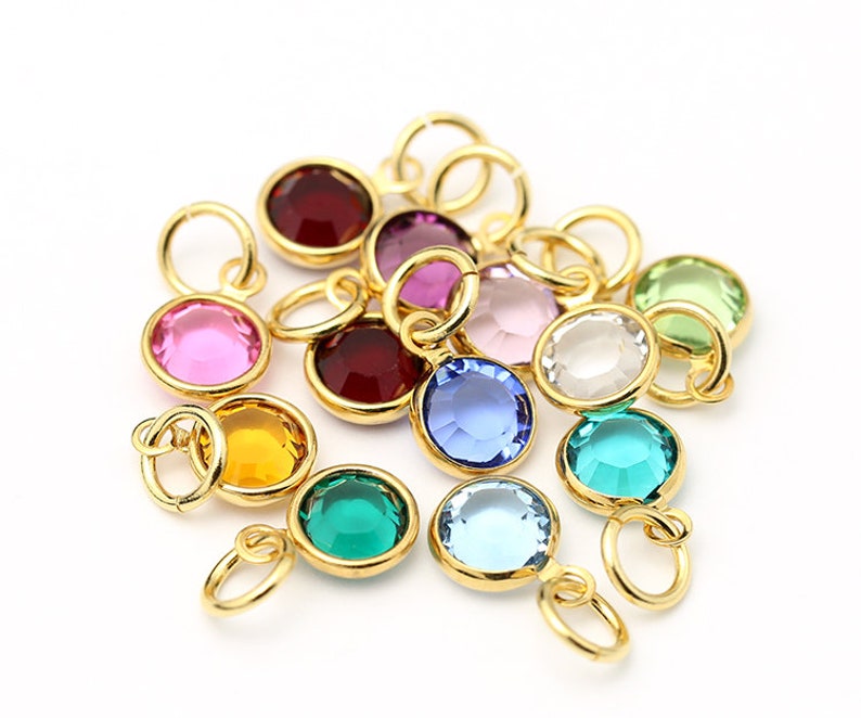 May include: Assortment of 12 gold-toned charms with colorful round glass stones. Each charm has a small loop for attaching to a necklace or bracelet.
