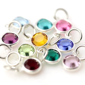 May include: Assortment of colorful crystal charms with silver settings. The charms feature round, faceted crystals in various colors, including purple, green, blue, pink, and yellow.