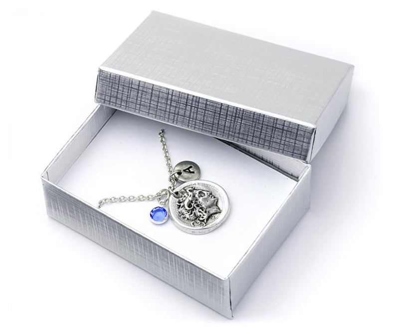 May include: A silver necklace with a blue gemstone charm and a silver charm with a woman's face and the letter A. The necklace is in a silver gift box.