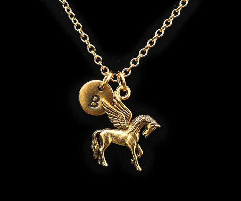 May include: A gold necklace featuring a winged horse pendant and a small round charm engraved with the letter "B".
