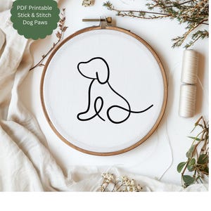 May include: A white embroidery hoop with a black line drawing of a dog sitting. The text "PDF Printable Stick & Stitch Dog Paws" is in a green circle at the top of the image.