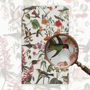 May include: A rectangular, floral-themed fabric with a vintage bird and flower pattern. The design features various birds, red and orange flowers, and green foliage on a white background. A magnifying glass is in the foreground.