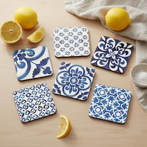 May include: A collection of square coasters with various blue and white floral and geometric patterns. The coasters are arranged on a light wooden surface, alongside lemons and a small bowl of salt. The coasters are a decorative home accessory.