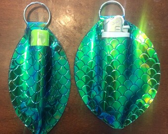 May include: Two green iridescent keychains with a mermaid scale pattern. One keychain has a small green tube of hand sanitizer inside and the other has a silver lighter inside.