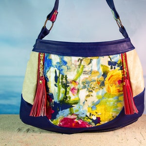 May include: A blue and beige shoulder bag with a floral print and red tassels. The bag has a zipper closure and a top handle.