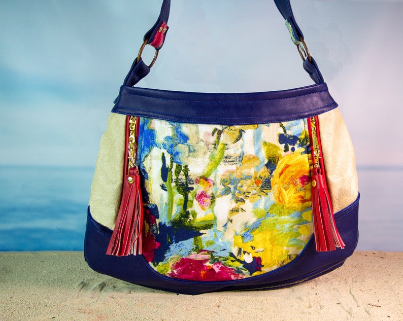 May include: A blue and beige shoulder bag with a floral print and red tassels. The bag has a zipper closure and a top handle.