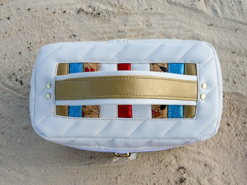 May include: White quilted leather cosmetic bag with a gold handle and colorful striped fabric accents. The bag has a zipper closure.