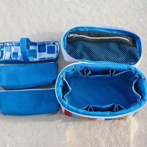 May include: A set of four blue and white zippered pouches, including a large oval-shaped pouch with multiple compartments and a mesh pocket. The pouches are made of fabric and have a white zipper.