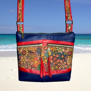 May include: A blue crossbody bag with a red strap and a floral print. The bag has two zippered pockets and a tassel.